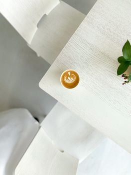 Top view of latte with coffee art on a white table, minimalist design.
