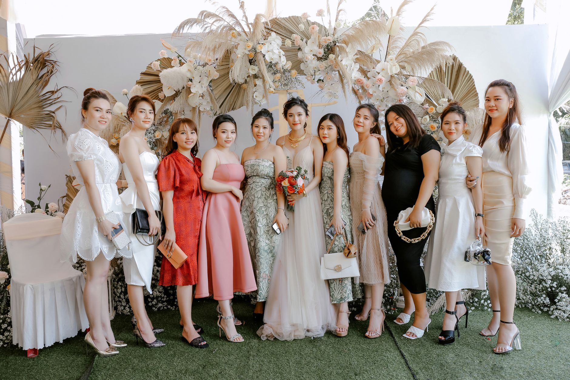 Smiling Asian woman in elegant dress standing near friends and looking at camera after wedding ceremony