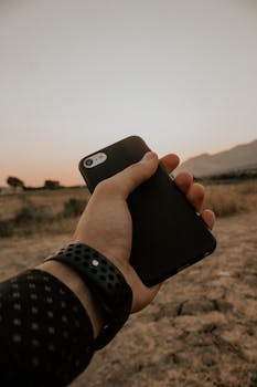 A person holding a smartphone outdoors at sunset, showcasing modern technology in nature.