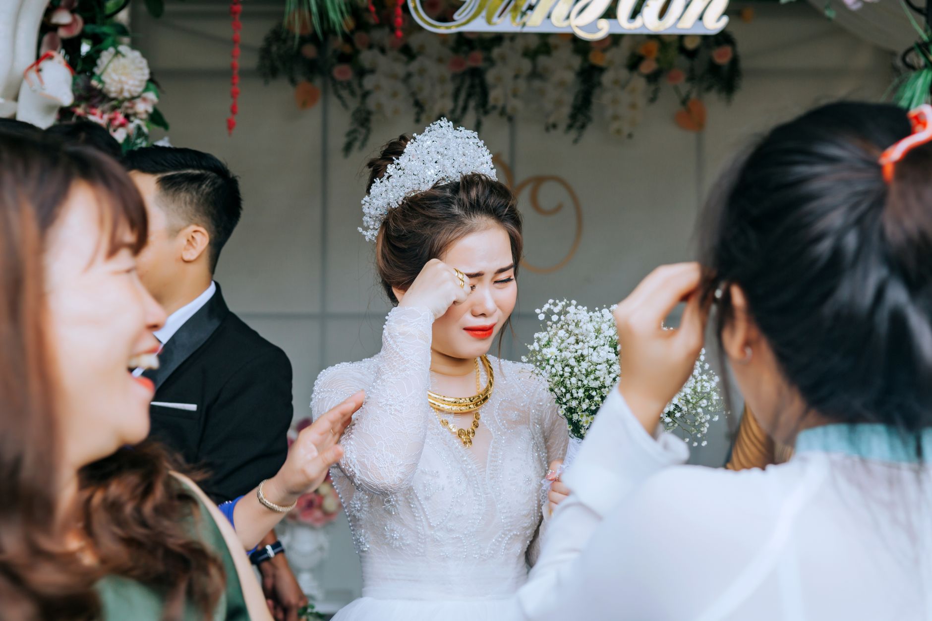 Elegant Asian woman in elegant wedding apparel standing with guests and crying from happiness