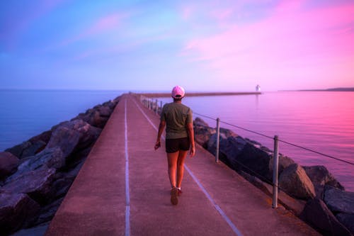 A Person Walking on a Concrete Pathway during Sunset