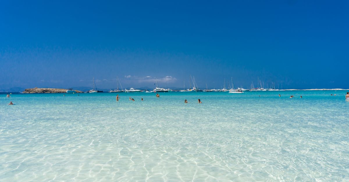 Enjoy leisure time at a Spanish beach with turquoise waters and distant yachts, perfect for summer vacation.