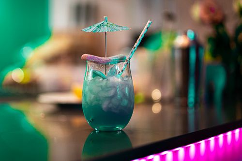 Free A vibrant blue cocktail with ice, a small umbrella, and candy garnish, set on a reflective bar surface. Stock Photo