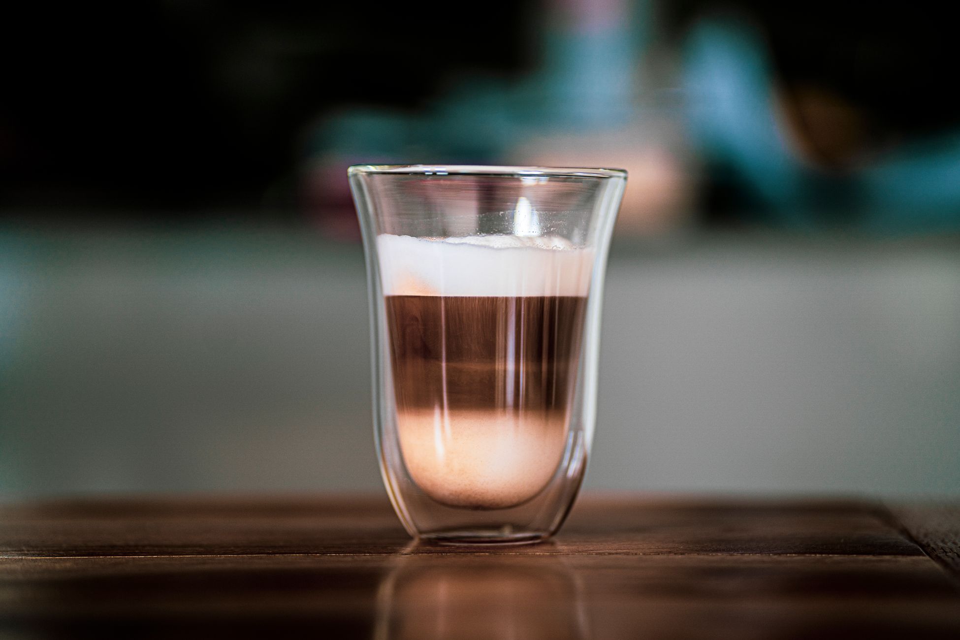 Close-up of a cappuccino with foam layers in a sleek double-walled glass on a wooden table.