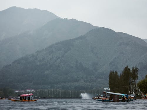 Mountains in fog against lake with roofed boats