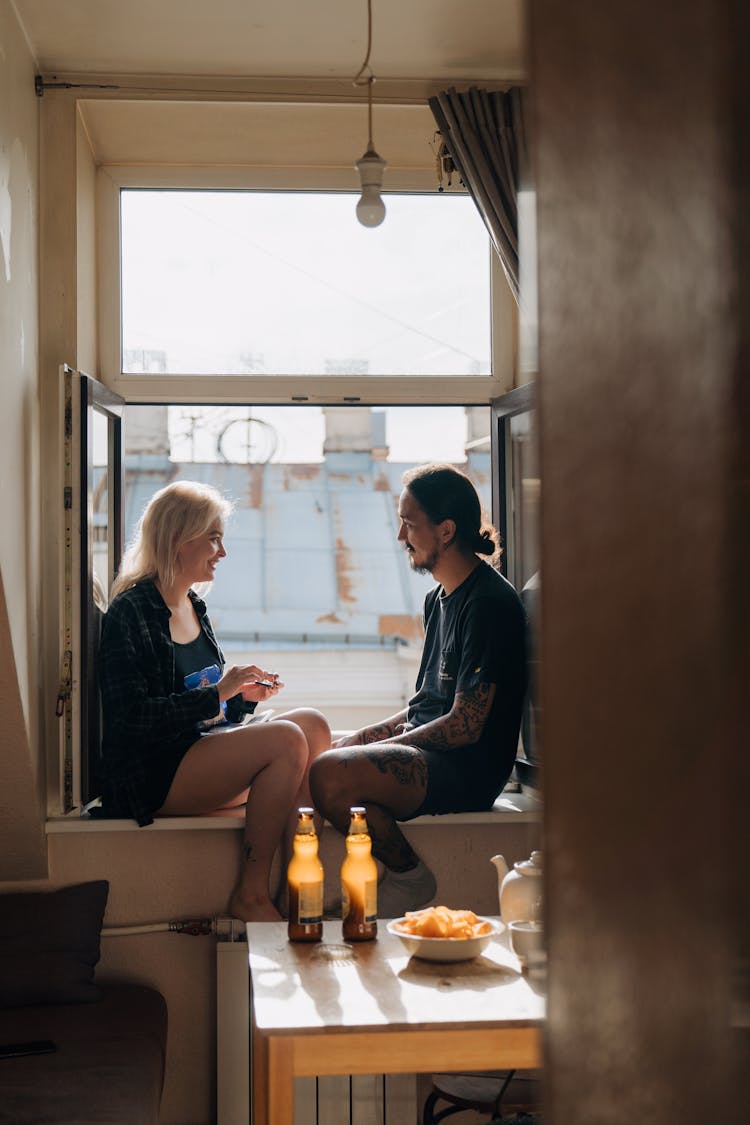 A Couple Hanging Out Together At Home Sitting On The Windowsill