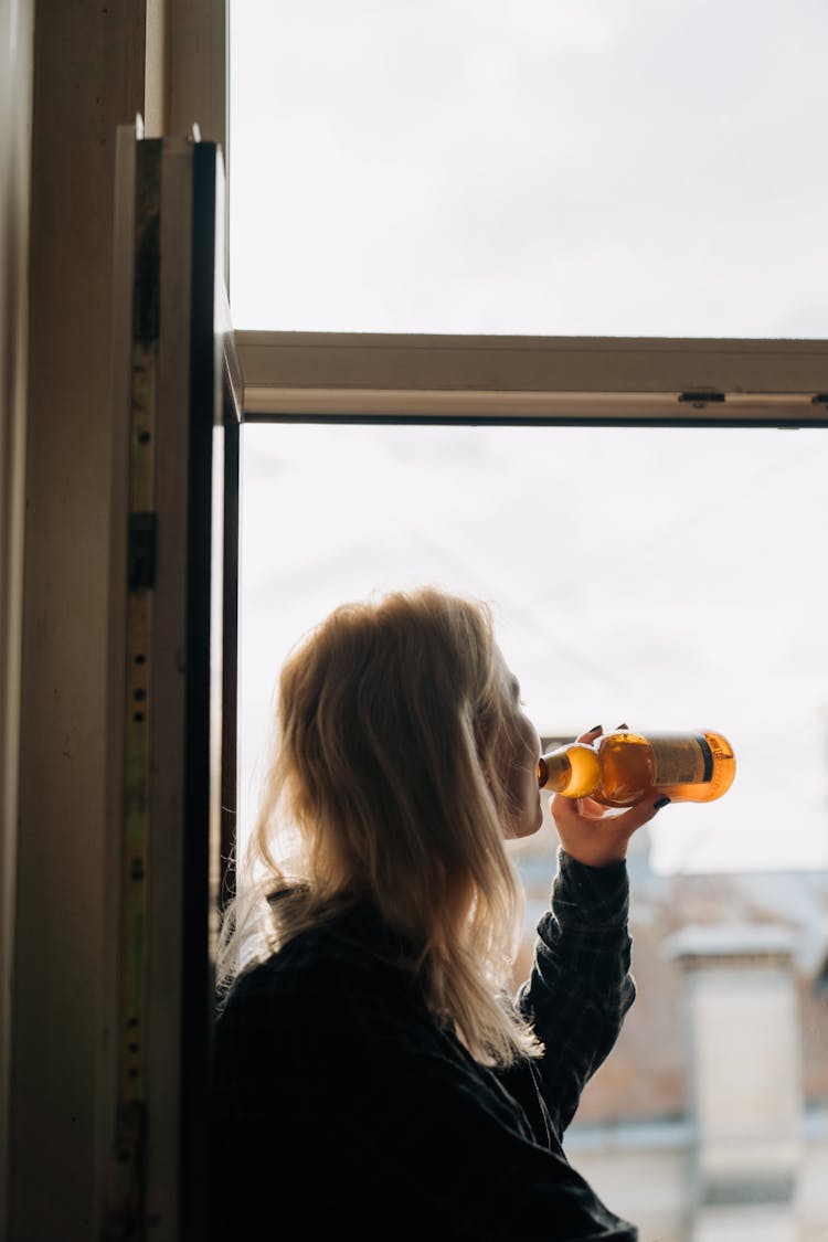 A Blonde-Haired Woman Drinking A Bottle Of Beer