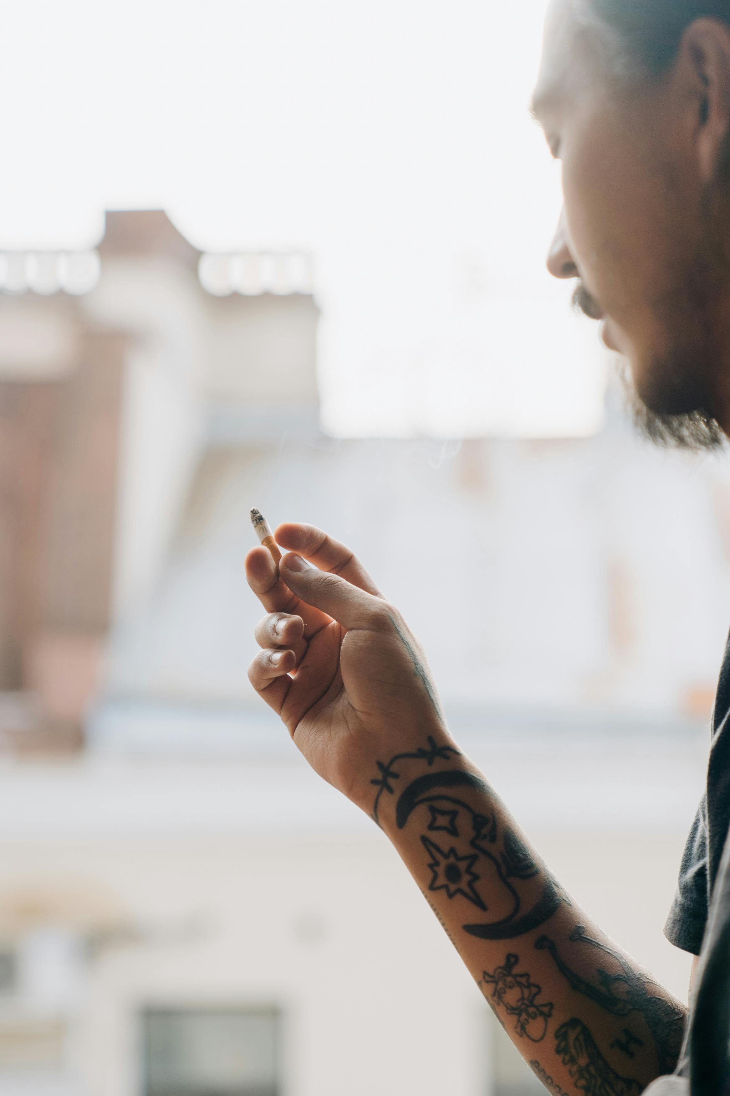 Crop ethnic hipster man smoking cigarette on balcony ?? Free Stock Photo