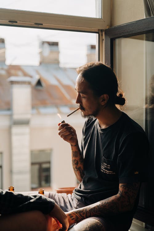A Man Lighting a Cigarette while Sitting by the Windowsill