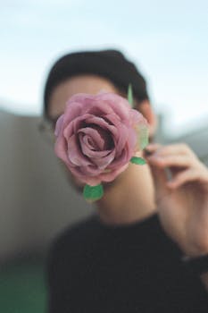 Faceless portrait of a person holding a vibrant pink rose outdoors.