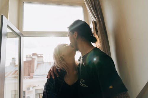 A Man and Woman Kissing Near Window