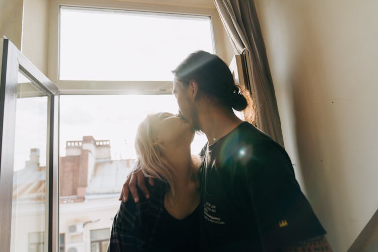 A Man And Woman Kissing Near Window