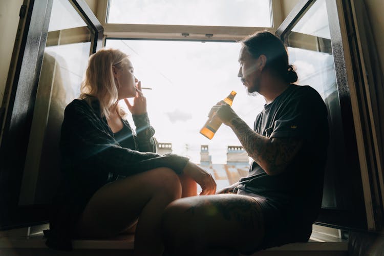 A Couple Smoking And Drinking By A Window