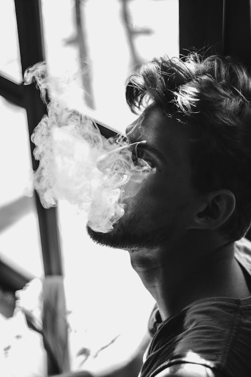 Grayscale Photo of a Man Exhaling Smoke