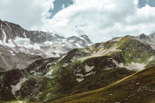 Picturesque scenery of rocky mountains with snow and grass under cloudy sky in daytime