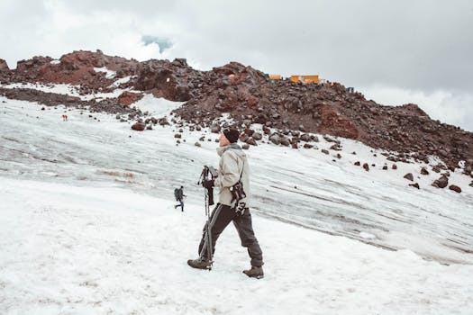 Full body of male traveler in warm outerwear walking with trekking sticks on snowy mountain ridge in daytime