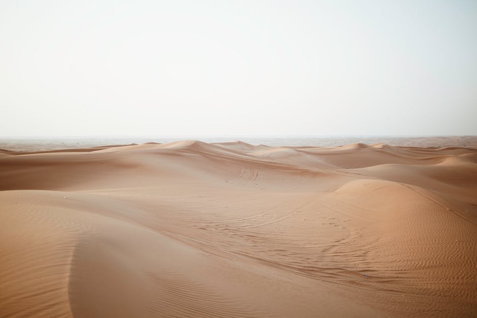 Picturesque view of endless sandy dunes in dry desert under cloudy sky in daylight
