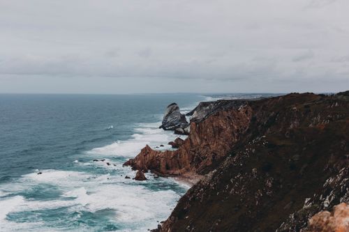 Free Picturesque scenery of rough rocky cliffs near foamy waves on blue sea in cloudy weather Stock Photo