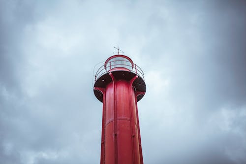 From below of red metal lighthouse on lonely surface under cloudy sky in daylight