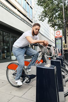 Young man sitting on a rental bike in a bustling London street, showcasing modern urban lifestyle.