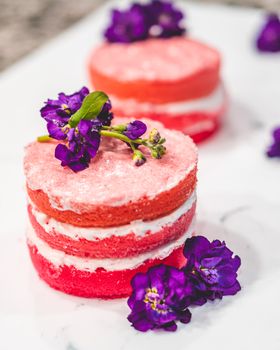 Beautiful pink layered cakes topped with vibrant purple flowers, creating a stunning dessert presentation.