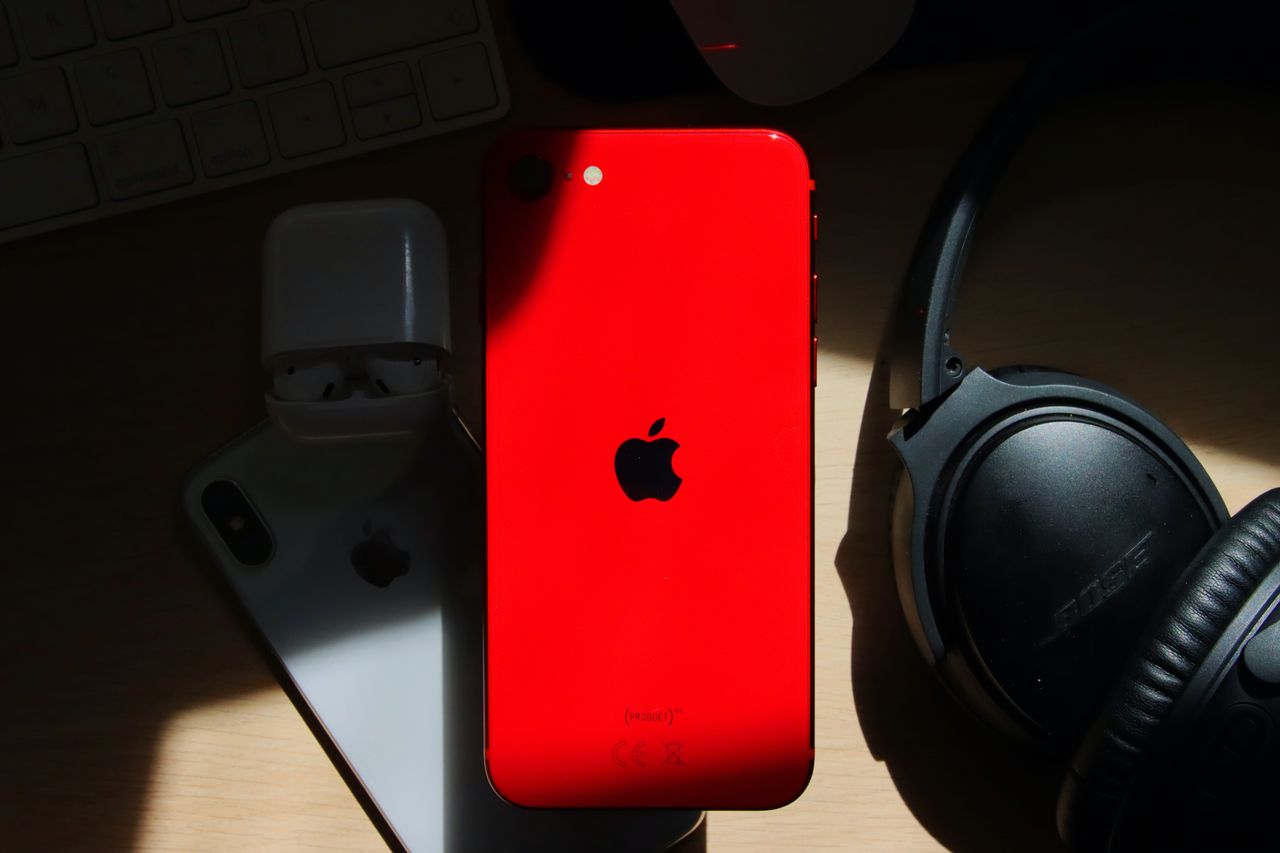 a flat lay of a red iphone surrounded by airpods and bose headphones o