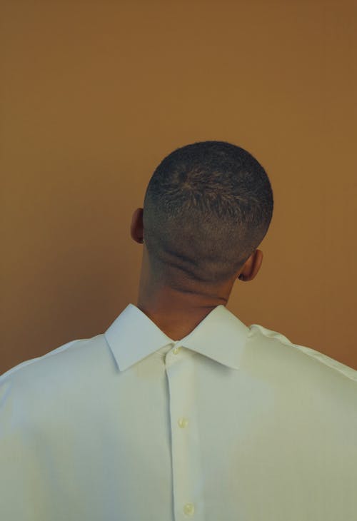 Back view of African American male with short hair wearing white clothes and posing in front of beige background