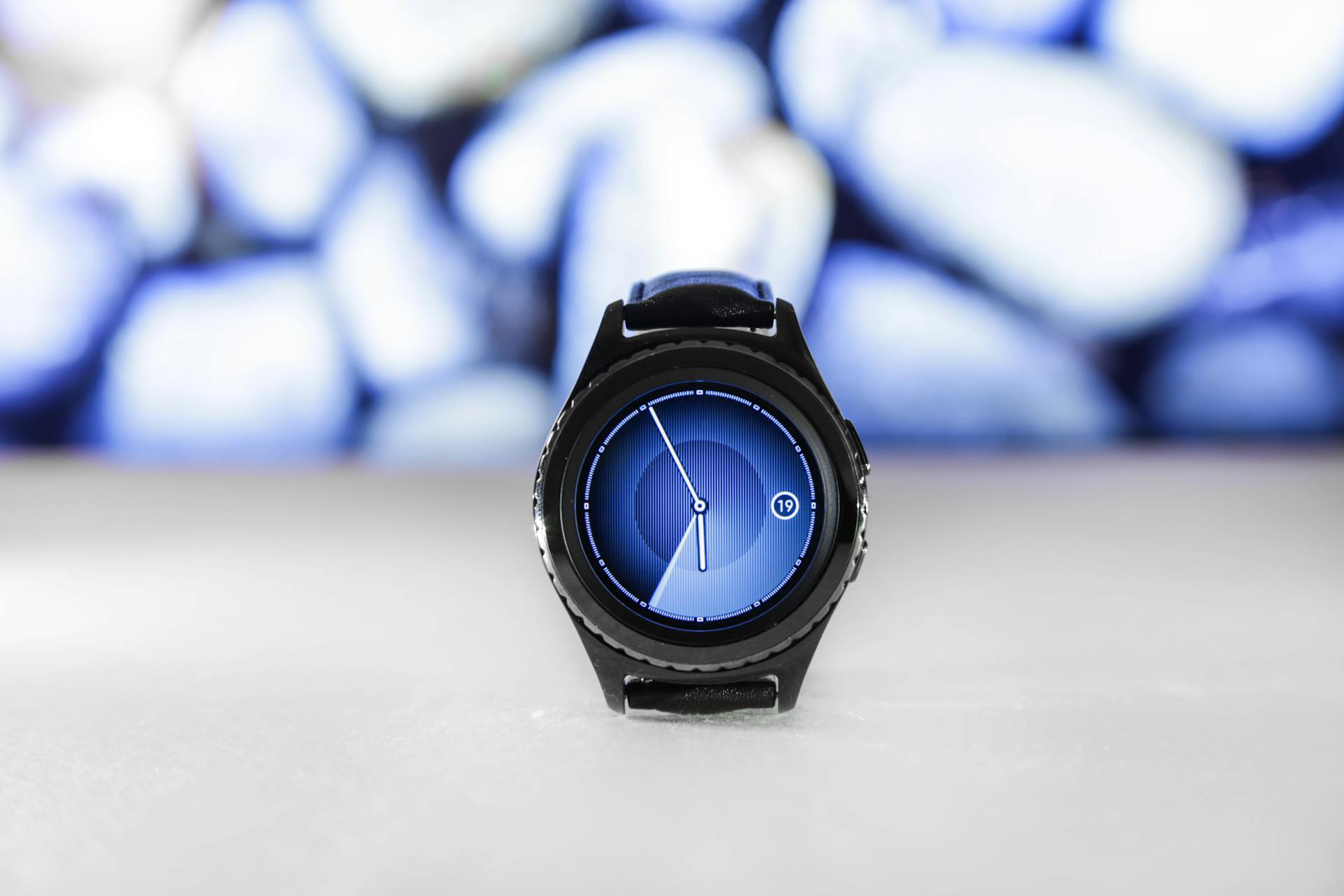 A sleek digital smartwatch with a blue interface against an abstract blurred background. Stylish and modern.