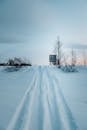 Perspective view of narrow wheels traces on snowy frozen valley with leafless trees under blue sky in winter countryside