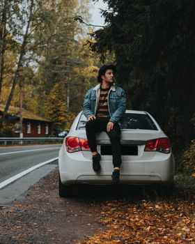 一名男子穿着牛仔布和软呢帽，坐在停在森林道路上的汽车里