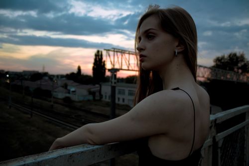 Free Stylish woman in black dress leaning on railing at sunset, evoking a moody and trendy vibe. Stock Photo