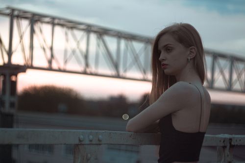 Free A fashionable young woman leans on a railing, set against a sunset backdrop with a blurred cityscape. Stock Photo