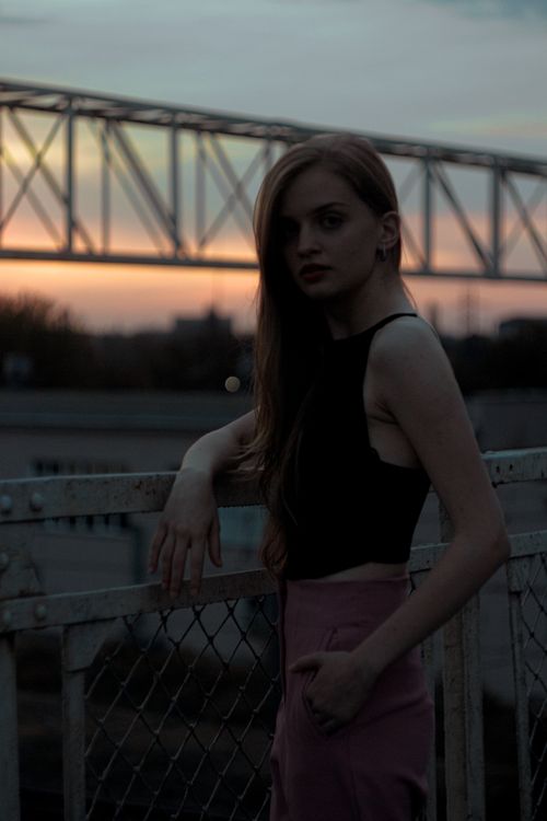 Free Portrait of a fashionable young woman leaning on a railing during a dramatic sunset in the city. Stock Photo