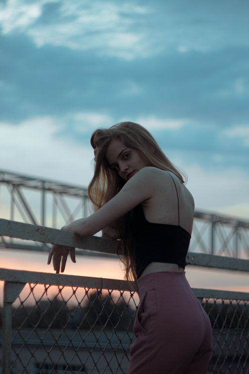 Free Caucasian woman posing stylishly on a railing during sunset, showcasing modern fashion. Stock Photo