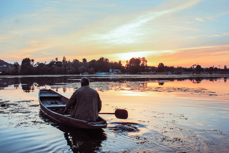 Faceless Mature Man Floating In Boat On Lake In Evening