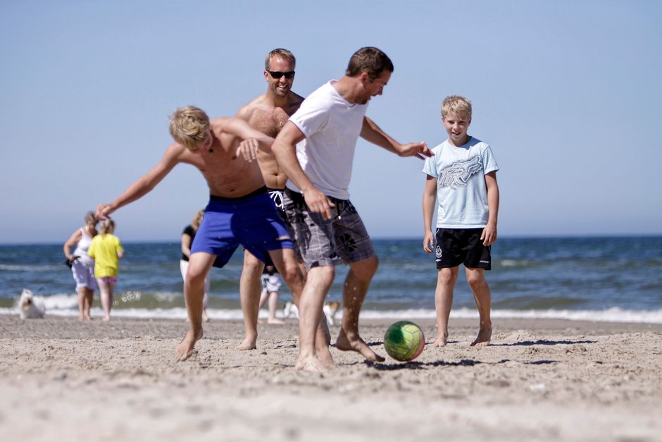 Group of friends enjoying football on a sunny beach in Denmark, capturing joy and bonding.