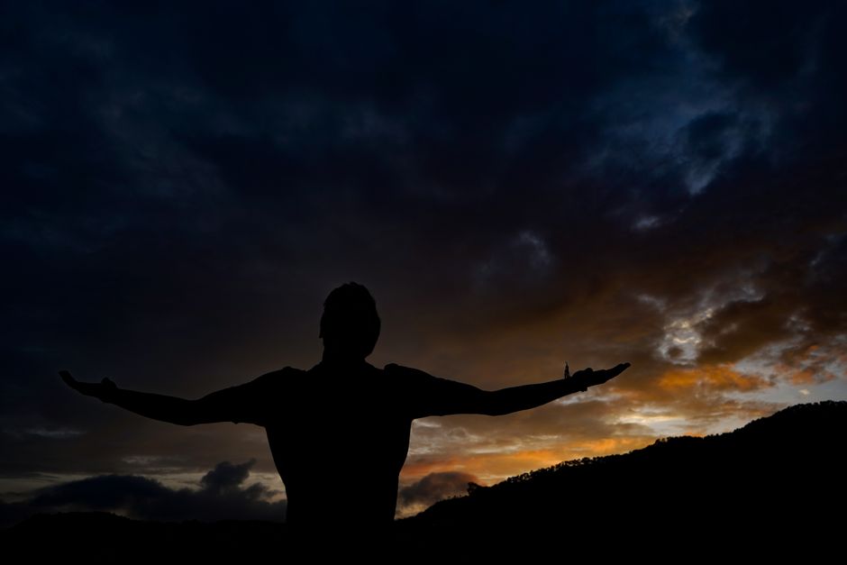 A silhouette of a person with arms outstretched against a vibrant sunset sky.