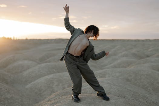 A man in a suit poses shirtless against a desert backdrop during sunrise, capturing a blend of fashion and nature.