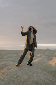 A man in a suit poses dramatically on a sandy desert landscape at dawn, embracing contemporary fashion and art.