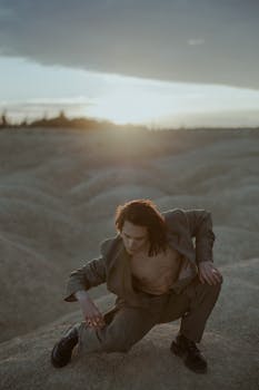 A man in a stylish suit poses against a desert backdrop during sunset, evoking a minimalist and dramatic mood.