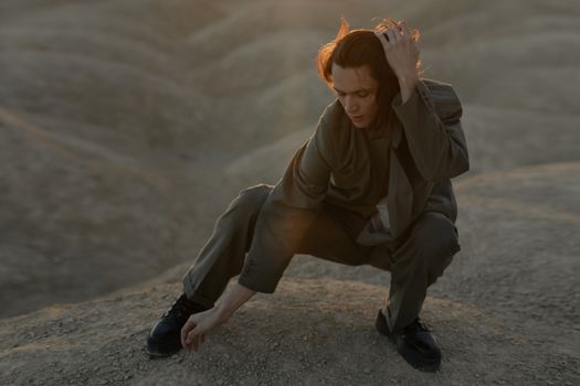 一个穿着西装的男人在温暖的傍晚光线下，于干燥而尘土飞扬的风景中艺术地摆着姿势