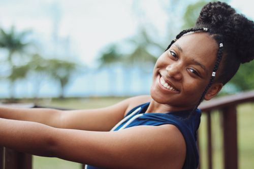Free Side view of crop young cheerful ethnic female with Afro braids looking at camera near wooden fence Stock Photo