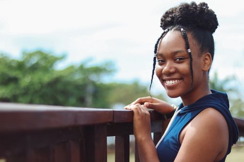 Free Side view of young content black female in trendy wear looking at camera near wooden fence under sky Stock Photo
