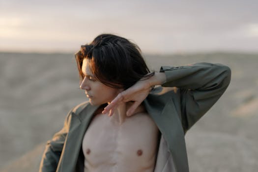 A shirtless man posing artistically in a green blazer in a sandy desert setting.