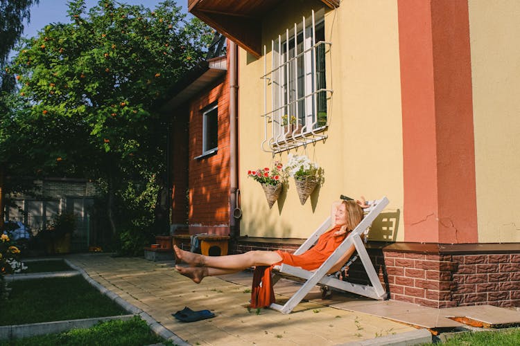 A Woman Sunbathing While Sitting On A Reclining Chair Outside Her House