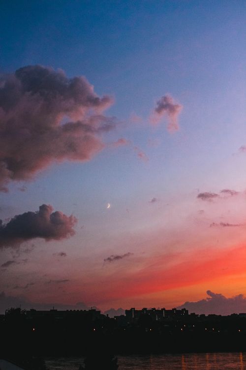 Free Spectacular city silhouette against a dramatic sky with vibrant sunset hues and scattered clouds. Stock Photo