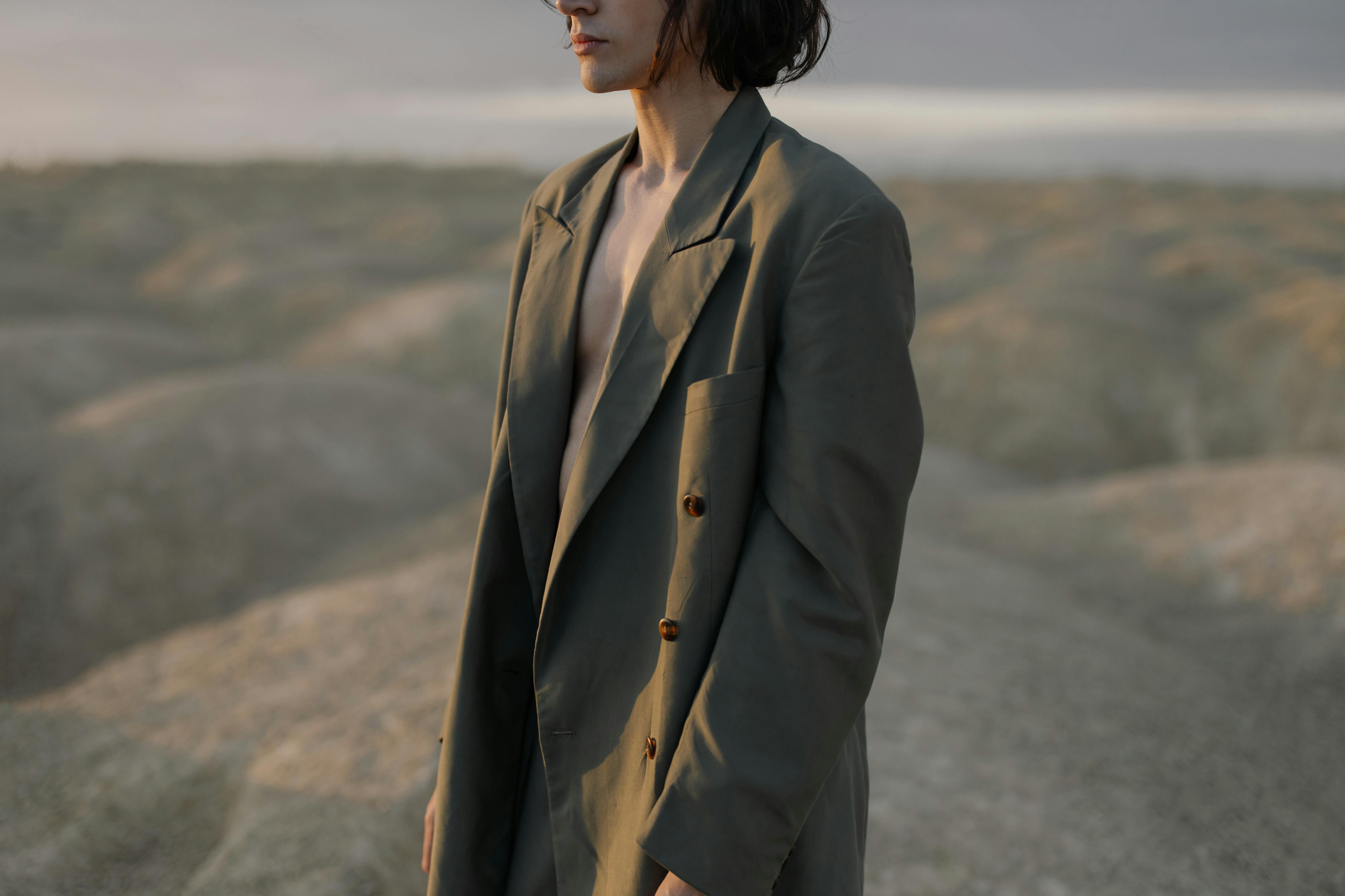 woman in brown coat standing on gray sand