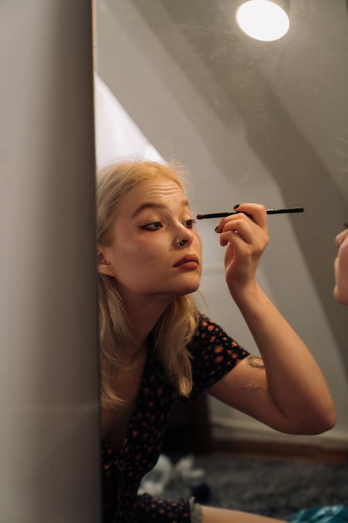 A Reflection of a Young Woman Putting on Makeup