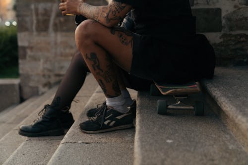 Free A Person with Tattoos Sitting on a Skateboard Stock Photo