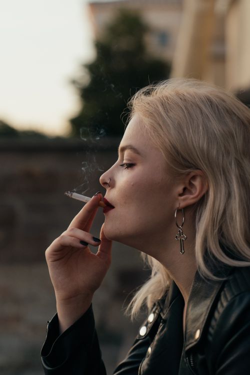 Free Profile of a woman smoking a cigarette, wearing a leather jacket and cross earring. Stock Photo